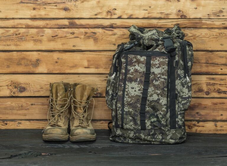 Tactical backpack and pair of hiking boots against a wooden background Tactical backpack and pair of hiking boots against a wooden background