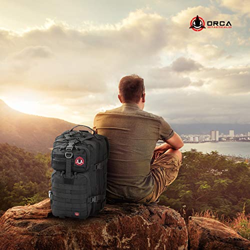 Wide angle view of man sitting on a boulder watching the sun set over the landscape, with a black tactical backpack by his side