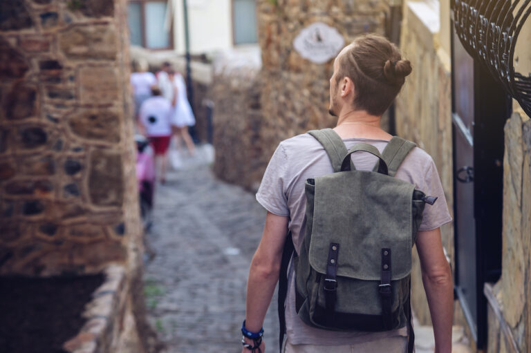 Man wearing tactical backpack walking through old town street Man wearing tactical backpack walking through old town street