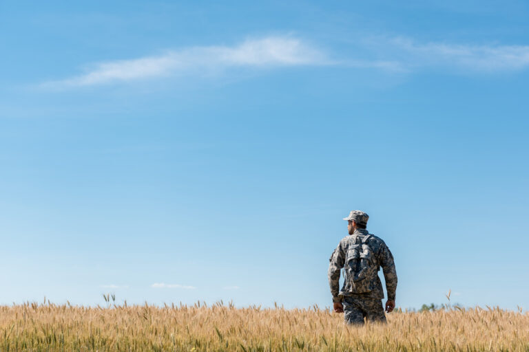 Military man wearing tactical backpack in golden field Military man wearing tactical backpack in golden field