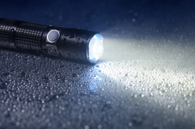 Black tactical flashlight illuminating wet surface Black tactical flashlight illuminating wet surface