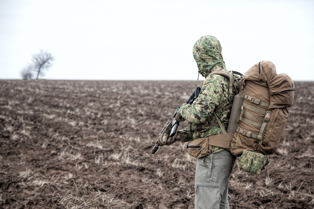 Man wearing tactical gear, standing in a barren field